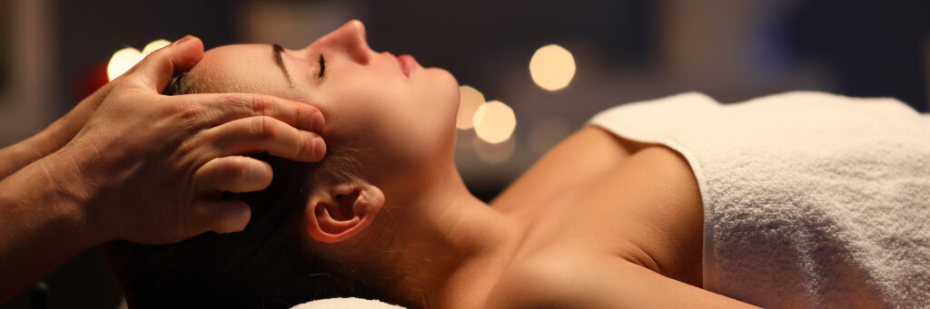 Vrouw ligt op de bank op haar rug met gesloten ogen en geniet van een hoofdmassage.